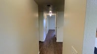 This two-story space offers a functional and practical layout designed for comfortable everyday living. The interior is defined by rich, dark hardwood-style plank flooring that runs throughout, providing a warm and grounded aesthetic that contrasts cleanly with the light-toned walls.

A central hallway serves as the main artery of the floor plan, connecting multiple rooms and providing clear sightlines from one end of the space to the other. The corridor is lined with multiple doorways leading to individual rooms, offering a well-organized and efficient use of space. White interior doors and clean white trim throughout contribute to a crisp, uniform finish.

Overhead lighting fixtures are positioned along the hallway ceiling, ensuring consistent illumination through the interior. Ventilation is provided via ceiling-mounted HVAC vents, indicating a central air system in place.

The light-colored walls throughout the space create a neutral backdrop that allows for versatile interior styling. The overall ambiance is clean, simple, and move-in ready, with an emphasis on practicality. Spanning two floors, this space provides ample room for a variety of uses, with the multi-level design allowing for clear separation between living and private areas.