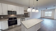 Located at 4205 Third Ave S in Birmingham, Alabama, this single-floor residence offers a thoughtfully designed, contemporary living space with modern finishes throughout. The open-concept kitchen serves as a central highlight, featuring crisp white shaker cabinetry, granite countertops, a textured tile backsplash, and a full suite of stainless steel appliances including a range, microwave, dishwasher, and refrigerator. A center island with matching granite provides additional prep space and is illuminated by a trio of stylish pendant lights. Wood-style luxury vinyl plank flooring flows throughout the main living areas, lending warmth and continuity to the space. The living area is bright and open, with recessed lighting and a clean, neutral palette that creates an inviting atmosphere. A bedroom features a ceiling fan, natural light from a window with blinds, and the same wood-style flooring, while an additional carpeted bedroom offers a softer, quieter environment with its own window view. The bathroom is well-appointed with a soaking tub and shower combo, accented by elegant marble-style tile surround and brushed nickel fixtures. Clean white walls and recessed lighting throughout contribute to a fresh, modern ambiance well-suited for comfortable everyday living.