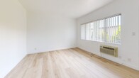 Located at 1011 E Palmer Ave in Glendale, CA, this single-floor, one-bedroom, one-bathroom unit offers a clean and functional layout finished with light wood-style flooring throughout. The open kitchen and living area features warm-toned cabinetry, stainless steel appliances including a gas range and full-size refrigerator, and crisp white walls that keep the space feeling bright and airy. The combined layout allows for flexible arrangement of living and dining furnishings. The bedroom is a comfortable size, appointed with a sliding double-door closet, a ceiling fan with light fixture, and a window fitted with vertical blinds that admits natural light and outdoor views. A wall-mounted HVAC unit provides climate control. The bathroom is neatly finished with light tile surrounding a full soaking tub and shower, a natural light-admitting window, and coordinating brushed nickel fixtures and accessories. Clean white walls and light hardwood-style flooring run consistently across the hallway and all rooms, lending a cohesive, modern feel throughout the unit. The overall aesthetic is minimal and well-maintained, making the space feel fresh and move-in ready.