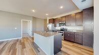 This single-floor residence offers a thoughtfully designed layout that balances functionality and modern aesthetics throughout. The kitchen serves as the focal point of the space, showcasing rich dark-stained cabinetry that extends to the ceiling for ample storage, granite countertops with subtle variation, and a full suite of stainless steel appliances including a French door refrigerator, electric range, and built-in microwave. A large central island with a granite surface and integrated sink provides additional workspace and casual dining potential. Recessed lighting illuminates the kitchen, which flows seamlessly into the open living area finished with wood-look plank flooring.

The bathrooms continue the design language established in the kitchen, featuring granite-topped dark vanities, chrome hardware, and wood-look tile flooring. One bathroom includes a soaking tub and shower combination, while another offers a walk-in shower with a clean white surround. The bedrooms feature plush carpeting and windows that invite natural light. A dedicated laundry area accommodates a full-size top-load washer and dryer. Neutral wall tones and consistent finishes create a cohesive, contemporary ambiance throughout.