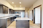 Located at 1117 S 21st Ct in Mount Vernon, Washington, this single-floor, 2-bedroom, 1-bathroom unit offers a thoughtfully designed layout with modern finishes throughout. The kitchen serves as the centerpiece of the home, showcasing rich dark cabinetry with sleek hardware, quartz countertops, a mosaic tile backsplash, and a full suite of stainless steel appliances including a refrigerator, range, microwave, and dishwasher. A substantial center island provides additional prep and storage space, complemented by recessed lighting overhead. Light wood-style flooring flows through the main living and kitchen areas, creating a warm and cohesive feel. The bedrooms are carpeted for comfort, with the primary bedroom offering a closet with built-in wire shelving and a natural light source through a window with views of the surrounding greenery. The second bedroom also features a window that brings in ample natural light. The bathroom is well-appointed with dark cabinetry, a quartz vanity countertop, and a stacked washer and dryer unit conveniently integrated into the space. The overall aesthetic is clean, contemporary, and functional, making this a comfortable and practical home.
