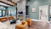 Located at 2700 Emerald Green Way in Knoxville, Tennessee, this thoughtfully designed single-floor community space offers a seamless blend of modern aesthetics and functional living. Rich hardwood flooring and exposed dark wood ceiling beams flow throughout the main corridor and living areas, establishing a warm yet contemporary tone.

The kitchen is a standout feature, boasting soaring ceilings, slate-blue cabinetry, open wooden shelving, a white subway tile backsplash, and a generously sized island with a white quartz countertop and woven bar seating. Pendant lighting and stainless steel appliances complete this well-appointed space.

The living room centers around a dramatic floor-to-ceiling stacked stone fireplace, flanked by built-in shelving. Globe pendant lights, teal-painted walls, and expansive seating areas create an inviting, social atmosphere. A separate lounge area with exposed beams and neutral furnishings offers a quieter retreat.

Two distinct dining areas serve different needs — one features a large conference-style table bathed in natural light from floor-to-ceiling windows, while the other offers an intimate round table with outdoor views through sliding glass doors. Black-framed glass partitions elegantly connect and define the various zones throughout, enhancing openness while maintaining purposeful separation.