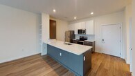 Located at 3900 W Broad St in Richmond, Virginia, this thoughtfully designed single-floor residence offers a contemporary living experience with clean lines and modern finishes throughout. The open-concept kitchen serves as the heart of the home, showcasing a striking two-toned design with dark lower cabinetry and crisp white upper cabinets. A spacious island with a steel-blue base and white quartz countertop provides both prep space and casual seating, while stainless steel appliances — including a refrigerator, electric range, and over-the-range microwave — add a polished, functional touch. A light blue herringbone tile backsplash introduces a subtle accent of color and texture. Warm hardwood-style flooring flows consistently through the main living areas, complementing the neutral, light-filled palette of the space. The bedroom features dual windows dressed with white blinds, allowing for ample natural light and views of the surrounding streetscape. The bathroom is equipped with a full soaking tub and shower combination, a vanity with dark cabinetry and white countertop, and clean tile flooring. An adjacent walk-in closet with wire shelving provides generous storage. Built-in shelving in the living area adds a practical and decorative element, completing this well-appointed, move-in ready home.