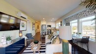 This thoughtfully designed single-floor residence offers a seamless open-concept layout connecting the living, dining, and kitchen areas. The living room features dark hardwood flooring, a wall-mounted split AC unit, recessed lighting, and large sliding glass doors that open to a private balcony, flooding the space with natural light and providing views of the surrounding neighborhood. The kitchen is outfitted with crisp white shaker cabinetry, neutral quartz countertops, stainless steel appliances including a range, over-the-range microwave, and refrigerator, making it both functional and stylish. Two well-proportioned bedrooms each feature a distinctive sage green accent wall, dark hardwood flooring, and large windows that invite generous natural light. The primary bedroom benefits from an en-suite bathroom with white cabinetry, a wide vanity with quartz countertops, and light wood-look tile flooring. A second full bathroom mirrors this clean, modern aesthetic. Throughout the residence, a cohesive design palette of whites, greens, and neutrals creates a bright, welcoming ambiance, complemented by contemporary finishes and thoughtful details at every turn.