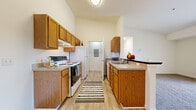 This single-floor unit in Holly, Michigan offers a practical and comfortable layout designed to maximize livability. The open-concept living and dining area is finished with neutral-toned carpet and connects seamlessly to the kitchen via a half-wall peninsula, creating a natural flow between spaces. A sliding glass door fills the living area with natural light and provides access to an outdoor space.

The galley-style kitchen features warm honey-toned oak cabinetry extending to the ceiling, offering generous storage. Light wood-style flooring, a double-basin sink, electric range, and a full-size refrigerator complete the functional cooking space.

The bedroom is a comfortably sized, carpeted retreat with a dedicated walk-in closet equipped with wire shelving and hanging rods. The full bathroom includes a single-sink vanity with oak cabinetry, tile flooring, and a shower/tub combination.

A separate laundry area accommodates a full-size washer and dryer and includes additional shelving. The entry foyer features a coat closet and a pendant light fixture, establishing a welcoming introduction to the unit's clean, neutral aesthetic throughout.