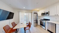 Located at 2430 Prospect St in Berkeley, CA, this thoughtfully designed unit offers four bedrooms, one bathroom, a kitchen, dining area, and a connecting hallway — all within a compact, efficiently utilized footprint. Light wood flooring flows consistently throughout every room, contributing to a clean, cohesive aesthetic.

Each bedroom features large windows that invite generous natural light and offer views of surrounding greenery. The rooms are designed with functionality in mind, accommodating a bed, wardrobe, and a dedicated desk and chair workspace — ideal for students or working professionals.

The kitchen is outfitted with modern stainless steel appliances, including a gas range, dishwasher, microwave, and refrigerator, complemented by white shaker cabinetry and quartz countertops. The dining area adjoins the kitchen and features a marble-top table, leather chairs, a wall-mounted television, and sliding glass doors that fill the space with natural light.

The bathroom is finished in a crisp, all-white palette with large-format wall tiles, a soaking tub with shower, a marble-topped vanity, and a small window for ventilation and light. The hallway connects the common areas to the private bedrooms seamlessly. Overall, the unit presents a modern, minimalist ambiance suited for shared living.