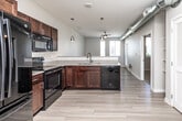 Located at 535 SW 11th St in Des Moines, Iowa, this one-bedroom, one-bathroom unit offers a well-organized layout across a single floor. The open-concept kitchen and living area forms the heart of the space, where light wood-look tile flooring extends throughout. The kitchen is equipped with rich dark-wood cabinetry, black appliances including a refrigerator, electric range, built-in microwave, and dishwasher, along with a double sink and light-toned countertops. Pendant lighting and exposed silver ductwork running along the ceiling add an industrial character to the space. The living area receives ample natural light from large windows and a glass-panel door that leads to a private balcony, offering views of the surrounding neighborhood. The bedroom features neutral carpet, a ceiling fan, and a window that continues the theme of natural light. A dedicated walk-in closet provides wire shelving and hanging storage. The full bathroom includes a dark-wood vanity with a single sink, a large mirror, wood-look tile flooring, and a soaking tub with shower. An open shelving unit near the hallway adds additional storage convenience throughout the unit.