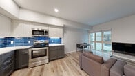 Located in Berkeley, CA (94720), this modern single-floor unit offers a thoughtfully designed open-concept layout that seamlessly connects the kitchen, dining, and living areas. The kitchen is a standout feature, showcasing a bold cobalt-blue subway tile backsplash that contrasts elegantly with two-tone cabinetry — white upper cabinets paired with charcoal gray lowers — and bright white countertops. A full suite of stainless steel appliances includes a refrigerator, dishwasher, electric range, and built-in microwave. Light wood-look flooring runs throughout the main living areas, contributing to a clean and contemporary aesthetic. The living space is well-proportioned, with large sliding glass doors and windows that invite natural light and provide views of the surrounding exterior. The bedroom features plush carpeting, multiple windows with horizontal blinds, a ceiling fan, and ample room for both sleeping and a dedicated study area with a desk. The full bathroom is finished in a crisp, all-white palette with a combined tub and shower, vanity, and matching wood-look flooring that ties the space together cohesively. Overall, the unit presents a functional and modern living environment well-suited for those seeking comfort and practicality.
