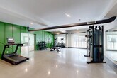 Located at 19 Hemans St in Worcester, MA, this fitness center offers a thoughtfully designed, single-floor layout encompassing a generous total area dedicated entirely to health and wellness. The main gym floor is the heart of the space, featuring polished concrete flooring that reflects the recessed lighting above. Bold green accent walls with geometric paneling create a vibrant, energizing atmosphere, while exposed ductwork along the ceiling adds an industrial character. The main area is outfitted with a comprehensive selection of cardio equipment — including treadmills, ellipticals, and stationary cycling bikes — alongside a multi-functional cable machine, a weight bench, and a full dumbbell rack, providing a well-rounded workout experience. Floor-to-ceiling mirrors line portions of the walls, enhancing the sense of space and supporting proper form during exercise. Large windows throughout admit ample natural light and views of the outdoors. A dedicated studio room features light wood flooring, soft mint-green walls, mirrored walls, a ballet barre, and exercise balls, making it ideal for yoga, stretching, or group fitness classes. A quiet study nook with built-in desks and ergonomic chairs offers a focused workspace. The facility is completed by a hallway and closet, ensuring practical organization and smooth circulation throughout.