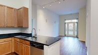 Located at 2301 Woodland Crossing Drive in Herndon, Virginia, this single-floor, 3-bedroom, 2-bathroom residence offers an efficiently designed layout with notable architectural details. The open-concept kitchen and living area serves as the heart of the home, featuring soaring ceilings with track lighting that enhance the sense of spaciousness. The kitchen is well-appointed with warm wood cabinetry, dark granite countertops, stainless steel appliances—including a gas range, microwave, and dishwasher—and a peninsula with an undermount sink, providing both prep space and a natural divider from the living area. Hardwood-style flooring runs throughout the main living spaces, adding warmth and continuity. The living room opens directly to a private balcony through glass French doors, allowing natural light and outdoor views to filter in. The three bedrooms are carpeted for comfort, each with neutral tones and windows offering natural light; one features an arched window detail. The two bathrooms are finished with white tile surrounds, wood-style flooring, and brushed nickel fixtures—one includes a glass-enclosed shower alongside a soaking tub. A hallway and closet complete the functional floor plan.