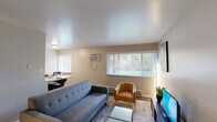 Located at 2890 S Ninth St in Kalamazoo, Michigan, this efficiently designed single-floor space makes excellent use of its compact footprint. The combined kitchen and living room serves as the heart of the unit, where natural light streams in through multiple windows offering views of surrounding greenery. The living area features wood-look flooring, a comfortable seating arrangement, a glass coffee table, and a wall-mounted TV, creating a welcoming and functional atmosphere. A wall-mounted air conditioning unit and baseboard heating ensure year-round comfort. The kitchen is outfitted with dark-toned cabinetry, white countertops, stainless steel appliances including a refrigerator and range, and wood-look flooring that carries through seamlessly from the living area. A dedicated office space provides a productive environment, complete with a large work desk, ergonomic seating, a ceiling fan with light fixture, and a window that brings in natural light. The bathroom is clean and modern, featuring dark wood cabinetry, a white countertop vanity, wood-look flooring, and a tub-shower combination. A hallway connects the rooms efficiently, contributing to the smooth flow throughout the space. Overall, the unit presents a neutral, contemporary aesthetic that is both practical and inviting.