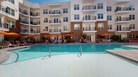 Located at 1027 Ashes Dr in Wilmington, NC, this outdoor amenity space is a well-appointed courtyard designed for relaxation and community living. At its centerpiece sits a large, crystal-clear swimming pool surrounded by an expansive pool deck finished in smooth gray pavers and warm wood decking. Vibrant orange umbrellas shade clusters of lounge chairs and seating areas, offering comfortable spots to unwind under the open sky.

The courtyard is framed on multiple sides by a multi-story residential building featuring a modern design that blends white paneling with exposed brick accents and private balconies that overlook the outdoor space. A covered pergola structure anchors one area of the deck, complemented by an outdoor bar and grilling station, making it ideal for social gatherings.

Thoughtfully designed landscaping adds greenery and texture throughout, with trees planted in mulched beds integrated into the paver deck, ornamental grasses, and manicured shrubs. A dedicated Wi-Fi Lounge with large glass doors connects the interior amenity space directly to the pool deck, ensuring seamless indoor-outdoor flow. The overall ambiance is bright, open, and resort-like, providing residents with an inviting outdoor retreat in the heart of Wilmington.