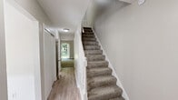 Located at Arbor Way in Ellington, Connecticut, this two-bedroom, two-bathroom home is thoughtfully laid out across two floors. The main level offers the larger footprint, featuring a kitchen equipped with oak cabinetry, granite-style countertops, a stainless steel sink, and white appliances. Adjacent to the kitchen, the dining room is bathed in natural light through a large window with wainscoting trim detail and durable hardwood-style flooring. The main level also includes a pantry, laundry area, and hallway leading to a carpeted staircase with white painted balusters. The upper level houses both bedrooms, each finished with plush carpet and baseboard heating. The spacious primary bedroom features vaulted ceilings, a sliding glass door opening to an outdoor view of lush greenery, and a closet. The second bedroom includes a closet and access to the stairwell. Two full bathrooms serve the home, each clean and simply appointed with a single-sink vanity and shower. Additional storage is provided by three closets throughout. Neutral tones, carpet on the upper level, and hard-surface flooring below create a cohesive, understated aesthetic throughout this efficiently designed home.