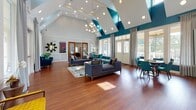 Located at 10002 Castile Ct in Henrico, Virginia, this single-story community clubhouse is designed to serve as a dynamic hub for residents. The open-plan common area anchors the space, showcasing soaring vaulted ceilings, rich hardwood flooring, and striking bold accent walls in deep navy and teal. A dramatic stacked-stone fireplace serves as a centerpiece, complemented by large arched windows that flood the interior with natural light and offer views of the surrounding greenery. The lounge area features comfortable seating arrangements and a modern chandelier, creating an inviting atmosphere for socializing.

The kitchen area is equipped with dark cabinetry, granite countertops, a stainless steel refrigerator, and a central island — ideal for community events. Adjacent café-style bistro tables positioned beside floor-to-ceiling draped windows provide a relaxed spot for casual gatherings.

The fitness center is a standout amenity, outfitted with cardio machines including treadmills and ellipticals, a full rack of dumbbells, and weight training equipment. Bright yellow accent walls, large windows, ceiling fans, and wall-mounted mirrors enhance the energetic atmosphere. Additional rooms visible in the layout suggest dedicated spaces for children's activities and other community uses, making this a well-rounded and versatile facility.