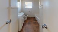 This single-floor home offers a practical and comfortable layout across several well-defined spaces. The living area is bright and welcoming, featuring warm hardwood-style flooring, a large sliding glass door that floods the room with natural light, and a seamless open connection to the kitchen. The kitchen is well-appointed with ample cream cabinetry, a tile backsplash, dark countertops, a double sink, a dishwasher, and a full-size refrigerator, all set on durable tile flooring. Adjacent to the kitchen, a dedicated utility room provides additional cabinet and counter space, with its own exterior door for convenient outdoor access. The bedrooms are generously sized, each featuring plush carpeting, bright windows with blinds, and ceiling-mounted ventilation. One bedroom stands out with a ceiling fan and light fixture, while another offers the added benefit of two side-by-side closets with built-in hanging rods, providing ample storage. The bathrooms are clean and functional — one features large-format tile flooring, a soaking tub, a single vanity, and a window, while the second includes a glass-door shower stall and a white vanity. Throughout the home, neutral tones and clean finishes create a cohesive and move-in-ready atmosphere.