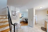 This two-story, two-bedroom, one-bathroom home offers a thoughtfully organized layout spread across two floors. The main level features a welcoming entryway with elegant marble-style tile flooring and a striking wrought-iron staircase, opening into a combined living and dining area. The living room is bright and inviting, anchored by warm hardwood floors, large windows with vertical blinds that allow generous natural light, and a cozy seating arrangement. The adjacent dining area provides a dedicated space for meals, while the kitchen is positioned conveniently nearby and equipped with standard appliances including a refrigerator. The upper level houses both bedrooms, each featuring hardwood floors, neutral white walls, and windows with blinds for natural light and privacy. The spacious primary bedroom offers a closet and comfortable proportions, while the second bedroom provides a functional and cozy retreat. The shared bathroom is clean and practical, featuring a wood-toned vanity with a white countertop, a large mirror, and a well-lit overhead fixture. Throughout the home, the consistent use of white walls, light-toned finishes, and hardwood flooring creates a cohesive, airy aesthetic that feels both functional and welcoming.