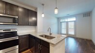 This well-appointed single-floor residence offers a thoughtfully designed layout with modern finishes throughout. The kitchen serves as a central highlight, featuring rich dark cabinetry, light granite countertops, a classic white subway tile backsplash, and a full suite of stainless steel appliances including a refrigerator, range, and built-in microwave. A peninsula with an undermount sink and stylish pendant lighting above extends the workspace and creates a natural transition into the open living area. Hardwood-style flooring runs throughout the main living spaces, adding warmth and a cohesive aesthetic.

The living area benefits from natural light streaming through large sliding glass doors that open to an outdoor balcony, creating a bright and airy atmosphere. The bedroom is carpeted for comfort, features a ceiling fan, and is illuminated by natural light from a double window with blinds, offering a calm and restful retreat.

The bathroom is finished with the same attention to detail found throughout the unit, featuring dark cabinetry with a granite vanity top, hardwood-style flooring, a large mirror, and a full tub-shower combination enclosed in clean white subway tile. The overall design strikes a balance between modern style and everyday functionality.
