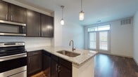 This well-appointed single-floor residence offers a thoughtfully designed layout with modern finishes throughout. The kitchen serves as a central highlight, featuring rich dark cabinetry, light granite countertops, a classic white subway tile backsplash, and a full suite of stainless steel appliances including a refrigerator, range, and built-in microwave. A peninsula with an undermount sink and stylish pendant lighting above extends the workspace and creates a natural transition into the open living area. Hardwood-style flooring runs throughout the main living spaces, adding warmth and a cohesive aesthetic.

The living area benefits from natural light streaming through large sliding glass doors that open to an outdoor balcony, creating a bright and airy atmosphere. The bedroom is carpeted for comfort, features a ceiling fan, and is illuminated by natural light from a double window with blinds, offering a calm and restful retreat.

The bathroom is finished with the same attention to detail found throughout the unit, featuring dark cabinetry with a granite vanity top, hardwood-style flooring, a large mirror, and a full tub-shower combination enclosed in clean white subway tile. The overall design strikes a balance between modern style and everyday functionality.