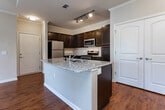 Located at 2310 Yellow Birch Way in Knoxville, Tennessee, this single-floor residence offers a well-designed open-concept layout that seamlessly connects the kitchen and living areas. The kitchen is a standout feature, showcasing rich dark espresso cabinetry extending to the ceiling, granite countertops, stainless steel appliances including a range, microwave, and refrigerator, and a large center island with a built-in sink — ideal for both cooking and casual dining. Track lighting illuminates the kitchen, while crown molding adds a refined architectural touch throughout. The living area is anchored by warm hardwood-style flooring, a ceiling fan with light fixture, and a tray ceiling detail that adds dimension. French doors lead to a balcony, filling the space with natural light and providing outdoor access. The bedrooms are carpeted for comfort, each equipped with ceiling fans and generous closet space. The bathroom features dark cabinetry, a wide vanity with light countertops, and a full tub-shower combination. Throughout the residence, neutral tones create a cohesive and inviting ambiance, making this a functional and attractive living space in the heart of Knoxville.