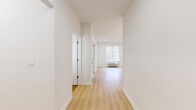 This thoughtfully designed single-floor unit offers a clean, contemporary aesthetic defined by crisp white walls, light wood-tone flooring, and an abundance of natural light throughout. A welcoming hallway connects the various rooms, creating a logical and efficient flow across the layout.

The kitchen stands out as a centerpiece of the space, showcasing two-tone cabinetry with forest green lower cabinets and white upper cabinets accented by gold hardware. A marble-look tile backsplash, white quartz countertops, a peninsula with bar seating, stainless steel appliances — including a gas range, microwave, refrigerator, and dishwasher — and elegant pendant lighting complete this well-appointed space.

Multiple living and sleeping areas offer generous proportions, each featuring large windows dressed with neutral roller shades that frame views of surrounding greenery. Wall-mounted HVAC units provide individual climate control in each room, and recessed lighting adds a polished finish overhead.

The bathroom features a full soaking tub with a tiled surround and brushed nickel fixtures, maintaining the clean, modern palette found throughout the unit. Every element of this space reflects careful attention to detail and a commitment to contemporary, functional design.