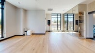 Located at 19 Centrepointe Drive in Ottawa's Centrepointe neighbourhood, this contemporary fitness and wellness facility offers a thoughtfully designed, generously proportioned space spread across a single floor. The exercise room is a standout, featuring slatted wood ceiling details, rubber sport flooring, and floor-to-ceiling black-framed windows that flood the space with natural light and provide views of the surrounding neighbourhood. The room is well-equipped with cardio machines including treadmills, ellipticals, and stationary bikes, alongside strength equipment such as a cable machine, power rack with free weights, and a full dumbbell rack. A decorative gold geometric screen partition adds an elegant architectural accent, dividing zones within the fitness area. The yoga and movement studio is equally impressive, boasting light hardwood flooring, full-length mirrors, and striking living green walls that introduce a natural, calming element. Large windows overlook a landscaped outdoor terrace. Together, the exercise room and living room-style studio create a cohesive, upscale wellness environment that balances high performance with refined design.