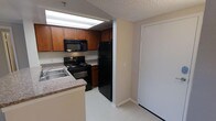 This single-floor residence offers a practical and well-organized layout designed for comfortable everyday living. The kitchen is a standout feature, equipped with warm wood-toned cabinetry that provides generous storage space. Black appliances, including a refrigerator, electric range, and over-the-range microwave, give the kitchen a cohesive and modern look. A double-basin sink is set into a laminate countertop, offering ample workspace for meal preparation. The kitchen flows naturally toward the entryway, where a full-size door opens to welcome residents and guests. The textured ceiling adds a classic residential touch throughout the space, while light-toned flooring lends a clean, bright feel to the interior. The overall layout is efficient and easy to navigate, with clear sightlines between the kitchen and the adjacent areas. The neutral color palette of beige and white walls creates a versatile backdrop that complements a variety of furnishing styles. This space is well-suited for those seeking a straightforward, functional home environment with all essential amenities thoughtfully arranged within a compact and efficient footprint.