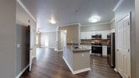 This single-story unit at 2202 W Texas St in Fairfield, CA presents a well-designed, open-concept layout with consistent neutral tones and quality finishes throughout. The kitchen serves as a central feature, showcasing white cabinetry, dark countertops, a peninsula with an undermount sink and contemporary faucet, and a full suite of stainless steel appliances including a refrigerator, electric range, and built-in microwave. Crown molding lines the ceiling, adding a refined architectural detail that carries through into the adjoining living areas.

Dark hardwood-style flooring flows through the main living spaces, complementing the warm, taupe-toned walls. The living room benefits from natural light through multiple windows with blinds and includes a ceiling fan. A separate entry area features two doors and transitions seamlessly into the main space.

Bedrooms are finished with plush carpeting and windows offering views of surrounding greenery. The bathrooms are appointed with wood-look flooring, white vanity cabinetry with stone-style countertops, and accessible grab bars in the bathtub/shower area. Overall, the unit offers a clean, functional, and comfortable living environment with cohesive design choices throughout.