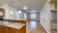 This single-floor residence offers a thoughtfully designed layout across two bedrooms and one bathroom. The open-concept kitchen and living area serves as the heart of the home, where warm-toned hardwood-style flooring flows seamlessly throughout. The kitchen features granite countertops, medium-toned wood cabinetry with modern hardware, a tile backsplash, a dishwasher, and a pendant light above the breakfast bar peninsula. Multiple windows fitted with horizontal blinds flood the living area with natural light and offer views of surrounding greenery.

The spacious primary bedroom includes direct outdoor access via a glass-paned door, a large window framing lush tree views, and a walk-in closet with double hanging rods and shelving. The second bedroom is carpeted and similarly bathed in natural light. The full bathroom is finished consistently with the kitchen, featuring a granite-topped vanity, wood cabinetry, a tub-shower combination, and a large mirror. Neutral beige walls and clean white trim maintain a cohesive, understated aesthetic throughout the residence.