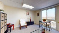 Located at 33 Labelle St in Highland Park, Michigan, this single-floor unit offers a well-organized and functional layout designed for comfortable everyday living. The main living area is finished with neutral carpet and warm beige walls, creating a welcoming atmosphere. Overhead fluorescent panel lighting provides consistent illumination, complemented by an abundance of natural light flowing in through large sliding windows that frame expansive outdoor views of the surrounding cityscape and skyline.

The living space flows naturally into a dedicated dining area, where a glass-top table and chairs sit adjacent to a floor-to-ceiling window framed by vertical blinds, offering an airy, elevated feel. Built-in storage and shelving units in the living area provide practical organization without compromising the open layout.

The kitchen is accessible directly from the living space and features warm wood cabinetry, a white countertop, and essential appliances, offering a compact yet fully equipped cooking area.

The bathroom is neatly appointed with tile flooring, a vanity with a wood cabinet base, a wall mirror, and a full bathtub with a shower curtain and white tile surround, providing all the essentials in a clean, functional setting.

Overall, this unit combines practical design with comfortable living spaces, elevated by natural light and pleasant outdoor views throughout.