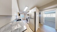 Located in Seattle's Capitol Hill neighborhood, this one-bedroom, two-bathroom residence offers a well-designed single-floor layout that maximizes every square foot. The kitchen is a standout feature, showcasing granite countertops, white shaker-style cabinetry, stainless steel appliances including a full-size refrigerator and range, and a skylight that floods the space with natural light. Light wood-style flooring runs through the kitchen and connects seamlessly to the adjacent dining area, which is brightened by a ceiling fan and window overlooking an outdoor space. The living room is generously proportioned for the overall footprint, featuring soft carpet, neutral gray walls, and a large picture window that allows ample natural light. The bedroom is carpeted and finished with neutral tones, offering a closet and direct hallway access. Two bathrooms serve the unit, one of which includes in-unit washer and dryer access — a practical and convenient feature. Both bathrooms are cleanly finished with light flooring and neutral walls. Hallways connect each room efficiently, contributing to a logical and functional flow throughout. The overall aesthetic is modern and understated, with consistent neutral tones and updated finishes throughout.