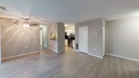 This single-story residence is designed with a practical, open-concept layout that promotes a seamless flow between the main living areas. The living room is generously sized, finished with durable wood-look flooring in a neutral gray tone, and features a sliding glass door fitted with vertical blinds that allows natural light to filter in while providing access to the outdoors. The space connects openly to a dining area and kitchen, creating an inviting, cohesive atmosphere throughout.

The kitchen is well-equipped with stainless steel appliances, including a refrigerator and an electric range, complemented by white shaker-style cabinetry, dark granite-style countertops, and a mosaic tile backsplash that adds a contemporary accent. A pass-through counter connects the kitchen to the adjacent dining or living space. In-unit laundry hookups are also accessible from within the kitchen area.

The bedrooms are carpeted for comfort and feature neutral taupe walls with ample natural light provided by large windows with blinds. One bedroom includes direct access to a private bathroom with a wide vanity, large mirror, and bright vanity lighting. A second full bathroom features a tub and shower combination with tile surround and brushed nickel fixtures, maintaining a clean, functional aesthetic throughout.