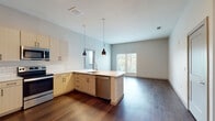 This single-floor residence showcases a thoughtfully designed open-concept layout where the kitchen flows seamlessly into the living area. The kitchen is outfitted with light wood cabinetry, a classic white subway tile backsplash, and a full suite of stainless steel appliances, including a French door refrigerator, electric range, built-in microwave, and dishwasher. A peninsula with pendant lighting overhead provides additional workspace and serves as a natural divider between the kitchen and the spacious living area, which benefits from natural light streaming through large windows with views of surrounding greenery.

Rich, dark hardwood-style flooring runs throughout the main living spaces, creating a warm contrast against the light blue-gray walls. The bedrooms feature plush carpeting and windows with outdoor views, offering a quiet retreat. A generously sized walk-in closet with wire shelving provides ample storage.

The bathrooms are finished with clean, modern details. The primary bathroom includes an expansive vanity with a light wood base, white countertop, and backlit mirror, while a secondary bathroom features a subway tile tub surround and matching wood-toned cabinetry. The overall aesthetic is cohesive, contemporary, and move-in ready.