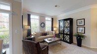 Located at 3280 Mill Run Dr in Hilliard, Ohio, this single-floor residence offers a thoughtfully designed layout with a comfortable, neutral aesthetic throughout. The living room serves as the heart of the home, featuring crown molding, plush carpeting, and an abundance of natural light streaming through large windows dressed with elegant dark curtains. The open flow connects seamlessly to the dining area, which is highlighted by a glass-top table and a sliding glass door that provides direct access to the outdoors and pleasant views of the surrounding community. The kitchen is well-equipped and visually striking, boasting white cabinetry, granite-style countertops, a large center island with bar seating, pendant lighting, hardwood-style flooring, and a full suite of appliances including a dishwasher. The bedroom is generously proportioned with soft carpeting, ample wall space, and a walk-in closet offering organized storage. Two full bathrooms serve the residence — each finished with granite-topped vanities and tub/shower combinations with tile surrounds. The overall ambiance is warm and inviting, with consistent neutral tones, crown molding accents in the main living areas, and an abundance of windows that keep the space feeling bright and open.