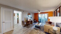 This single-floor residence combines contemporary design with vibrant personality throughout its well-appointed layout. The living area serves as the heart of the home, featuring wood-style flooring, a bold orange accent wall, and a ceiling fan overhead. A sliding glass door floods the space with natural light and opens to a private balcony with outdoor views, while a dedicated console area with a round mirror adds a functional yet decorative touch. The open flow connects seamlessly to the dining area and kitchen, where crisp white shaker cabinets, dark countertops, a classic subway tile backsplash, and stainless steel appliances — including a refrigerator and range with overhead ventilation — create a clean, functional cooking space. Two bedrooms provide comfortable retreats, each finished with plush carpet, ceiling fans, and windows dressed with sheer curtains. Both rooms feature striking teal accent walls that lend a bold, modern character, with ample space for furnishings. The bathroom is neatly appointed with a combined tub and shower, a curtained rod, dark countertop vanity, and wood-style flooring that carries through from the main living areas. Throughout the residence, a cohesive use of warm neutrals and vibrant accent colors creates a dynamic yet inviting ambiance.