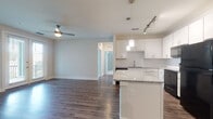 This single-story residence offers a thoughtfully designed open-concept layout that seamlessly connects the kitchen and living area. The kitchen is a standout feature, equipped with white shaker-style cabinetry, granite countertops, a subway tile backsplash, and black appliances including a range, microwave, and refrigerator. A central island with matching granite provides additional workspace and casual dining options, while pendant lighting and a track light fixture illuminate the space effectively. Dark hardwood-style flooring extends throughout the main living areas, adding warmth and contrast to the light-toned walls.

The living area is generously proportioned, featuring a ceiling fan and open sightlines to the kitchen. Two carpeted bedrooms offer comfortable retreats, each with ceiling fans and natural light from windows with blinds. The primary bathroom features a glass-enclosed walk-in shower clad in large-format marble-style tile alongside a granite-topped vanity and tile flooring. A second bathroom includes a full soaking tub with a tiled surround. A dedicated laundry area accommodates a full-sized washer and dryer, completing the functional and well-appointed layout.