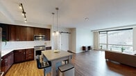 Located on the 15th floor at 811 S Washington Ave in downtown Minneapolis, this thoughtfully designed one-bedroom, three-bathroom residence offers a generous open layout with contemporary finishes throughout. The open-concept kitchen and living area serves as the heart of the unit, featuring rich hardwood-style flooring, exposed concrete columns, and large floor-to-ceiling windows that flood the space with natural light and frame sweeping city views, including a direct sightline to U.S. Bank Stadium. The kitchen is well-appointed with dark walnut cabinetry, stainless steel appliances, a subway tile backsplash, a center island with bar seating, and pendant lighting that adds warmth to the space. The living room extends naturally from the kitchen, offering an open and airy atmosphere with additional access to a private balcony. The bedroom is a comfortable retreat with plush carpeting, a built-in closet with shelving, and a large window showcasing iconic city landmarks. The three bathrooms are cleanly finished with subway tile surrounds, large-format floor tile, dark wood vanities with white countertops, and chrome fixtures. Two hallways connect the spaces efficiently, adding to the unit's well-organized flow throughout.