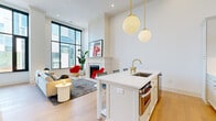 Located at 35 E Hubbard in the heart of Columbus, Ohio, this sophisticated one-bedroom, one-bathroom residence offers an impressive blend of modern design and refined finishes throughout. The open-concept kitchen and living area is the centerpiece of the home, boasting soaring ceilings that amplify the sense of space and light. Floor-to-ceiling black-framed windows flood the living room with natural light and frame dynamic urban views, while a classic white fireplace with a clean-lined surround adds warmth and character. The kitchen is thoughtfully appointed with white shaker cabinetry adorned with brass hardware, a white quartz waterfall island with seating, a gas range, stainless steel French-door refrigerator, white subway tile backsplash, and a striking brass faucet — all illuminated by globe pendant lights with gold accents. Wide-plank light hardwood flooring flows seamlessly throughout the entire residence. The bedroom is bright and airy, featuring a large black-framed window overlooking a terrace with greenery. A dedicated closet with built-in shelving and hanging rods provides organized storage. The bathroom features a dual-sink vanity with grey cabinetry, white quartz countertops, backlit mirrors, marble-look tile flooring, and a separate walk-in shower with full-surround tile.