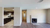 This single-floor residence offers a thoughtfully arranged layout connecting living, dining, and private spaces through a long central hallway. The living area is a standout feature, showcasing dark hardwood-style flooring, a classic fireplace with a tiled hearth, and recessed lighting that creates a warm, inviting atmosphere. A ceiling fan overhead adds both style and functionality to the adjoining dining or sitting area, which opens directly to the kitchen.

The kitchen is well-appointed with rich dark wood cabinetry, light granite-style countertops, stainless steel appliances including a dishwasher and range, and a double-basin sink — providing ample workspace and storage. Tile flooring runs throughout the kitchen, contrasting cleanly with the wood-style floors of the main living areas.

The bedrooms are comfortably sized, each featuring plush wall-to-wall carpeting, ceiling fans with light fixtures, and windows that bring in natural light. Closet space is accessible directly from the bedrooms. The bathrooms are finished with slate-toned tile flooring; one includes a full tub-shower combination with chrome fixtures, while another offers a separate toilet area. The overall design is clean, neutral, and move-in ready.