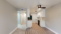 This single-floor residence offers a thoughtfully designed layout that balances functionality and comfort throughout. The kitchen serves as a standout feature, showcasing crisp white shaker-style cabinetry with matte black hardware, light quartz countertops, a black refrigerator, a dishwasher, and a undermount sink with a matte black faucet. Light wood-look flooring runs through the kitchen and living area, while a ceiling fan with an integrated light fixture provides both comfort and illumination. The open connection between the kitchen and living area creates a natural flow ideal for everyday living. The living space is generously proportioned, with soft neutral-toned carpet and a sliding glass door that invites natural light and provides access to an outdoor area with greenery views. The bedrooms are carpeted and finished in soft gray tones, each offering ample space and sliding-door closets with built-in hanging rods for organized storage. The bathroom is cleanly finished in white, featuring a vanity with a quartz countertop, a round mirror, and a full tub-shower combination with brushed nickel fixtures. Light wood-look flooring extends into the bathroom, tying the space together. Throughout, neutral gray walls and white trim create a clean, cohesive aesthetic.