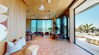 Located at 3401 S La Cienega Blvd in Los Angeles, this thoughtfully designed single-floor space blends warm natural materials with contemporary sophistication. The interior is defined by vertical slatted wood paneling that lines the walls, creating a cohesive and textural aesthetic throughout. Terracotta-toned tile flooring extends seamlessly from the entry area through the main space, contributing to the warm, earthy palette.

A striking terrazzo feature wall serves as a bold focal point in the kitchenette area, complemented by a fluted island, integrated cabinetry, and a pendant chandelier with sculptural metalwork. Track lighting and ambient ceiling fixtures provide layered illumination throughout.

The entry zone features a built-in wood bench with cushioned seating, a statement pendant light, and a folding glass door wall that opens fully to the exterior — flooding the space with abundant natural light and seamlessly connecting indoors to outdoors.

Floor-to-ceiling glass walls frame sweeping panoramic views of the Los Angeles skyline and surrounding hillsides. The expansive outdoor terrace extends the usable area significantly, offering generous lounge seating, an outdoor kitchenette, and unobstructed views under open skies — making it an exceptional setting for both intimate gatherings and larger events.