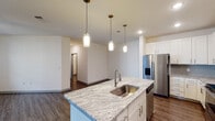This single-story, two-bedroom, two-bathroom residence in Houston, Texas offers a well-designed open-concept layout that seamlessly connects the kitchen and living area. The kitchen serves as a central focal point, showcasing a large granite-topped island with an undermount sink and elegant pendant lighting overhead. White shaker cabinetry extends to the ceiling, providing generous storage, while a tasteful subway tile backsplash, stainless steel appliances—including a French door refrigerator, range, microwave, and dishwasher—complete the space. Wood-style flooring runs throughout the main living areas, enhancing the modern aesthetic.

The living area benefits from natural light streaming through large windows and is equipped with a ceiling fan. Both bedrooms are carpeted and include ceiling fans, with natural light provided by windows with blinds. One bedroom features louvered bifold closet doors opening to a walk-in closet, while the other includes a standard closet.

Each bathroom is finished with granite-topped vanities and white cabinetry. One bathroom includes a soaking tub with tile surround and wood-style flooring. The second bathroom features a granite vanity and additional storage. The overall aesthetic is clean and contemporary throughout.