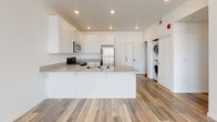 Located at 1122 Victorian Ave in Sparks, Nevada, this single-story unit offers a clean, modern design with a neutral color palette and practical layout. The kitchen serves as a central highlight, featuring white shaker-style cabinetry, granite-look countertops, and a full suite of stainless steel appliances including a refrigerator, electric range, and over-the-range microwave. A peninsula with an integrated sink provides additional prep space and separates the kitchen from the main living area. Wood-style plank flooring runs throughout the kitchen and living areas, adding warmth and durability to the space. Conveniently tucked near the kitchen is an in-unit laundry area with a stacked washer and dryer. The bedroom features plush carpet flooring and a sliding-door closet with a full-width hanging rod, providing ample storage. The bathroom is finished with white cabinetry, a generous vanity countertop, an oversized mirror, and wood-style flooring consistent with the rest of the unit. Recessed lighting throughout contributes to a bright, open atmosphere. The overall design is cohesive, functional, and move-in ready.