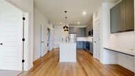 This 550 sq ft, 1-bedroom, 1-bathroom apartment at 200 Harvest Way in Argyle, TX features modern design with light wood-style flooring and a crisp white palette. The open kitchen/living area showcases gray shaker cabinets, white quartz countertops, stainless steel appliances, a kitchen island with pendant lighting, and an in-unit stacked washer/dryer. The 140 sq ft bedroom offers carpeted flooring, a ceiling fan, and natural light. The bathroom includes a gray vanity, LED mirror, and glass-enclosed shower. A spacious walk-in closet completes the unit.