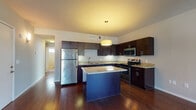 Located at 1643 E 118th St in Cleveland, Ohio, this single-floor residence offers a thoughtfully designed open-concept layout that seamlessly connects the living and kitchen areas. Rich, dark hardwood flooring flows throughout the main living spaces, complementing the warm, neutral tones of the interior.

The kitchen is a standout feature, showcasing dark espresso cabinetry, granite countertops, and a full suite of stainless steel appliances including a refrigerator, electric range, and built-in microwave. A central island with a granite surface and a bold navy-blue base provides additional prep space and serves as a natural focal point, accented by a modern pendant light overhead.

The living area is generously proportioned, bathed in natural light from large floor-to-ceiling windows and a glass door that opens to the outdoors. A ceiling fan adds both function and style to the space.

The bedrooms feature plush carpeting, ceiling fans, and windows that bring in ample natural light, creating comfortable and restful retreats. The bathroom is well-appointed with tile flooring, a dark vanity with granite countertop, a lighted mirror, and a shower-tub combination, with a small window providing natural ventilation. Overall, the unit presents a clean, modern aesthetic throughout.