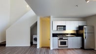 Located at 320 West Ash Street in the heart of downtown San Diego, this two-story unit offers a well-designed layout spread across two distinct levels connected by a carpeted staircase. The main living area features durable hardwood-style flooring that extends throughout the open space, lending a clean and contemporary feel.

The kitchen is thoughtfully appointed with white shaker-style cabinetry, dark countertops, and stainless steel appliances including a gas range with oven and a built-in microwave. A dedicated sink area completes the functional workspace, making the kitchen both practical and visually appealing. Adjacent to the kitchen, a convenient in-unit laundry area houses a full-sized washing machine, adding everyday practicality to the home.

The angled ceiling lines near the staircase area reflect the multi-level architecture, adding visual interest and a sense of character to the interior. A carpeted staircase with dark treads leads to the upper level, providing a smooth transition between floors. The overall palette of whites and neutral tones throughout the space creates a bright, airy atmosphere, making the home feel welcoming and move-in ready. This unit combines urban convenience with comfortable, well-equipped living in one of San Diego's most vibrant neighborhoods.