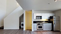 Located at 320 West Ash Street in the heart of downtown San Diego, this two-story unit offers a well-designed layout spread across two distinct levels connected by a carpeted staircase. The main living area features durable hardwood-style flooring that extends throughout the open space, lending a clean and contemporary feel.

The kitchen is thoughtfully appointed with white shaker-style cabinetry, dark countertops, and stainless steel appliances including a gas range with oven and a built-in microwave. A dedicated sink area completes the functional workspace, making the kitchen both practical and visually appealing. Adjacent to the kitchen, a convenient in-unit laundry area houses a full-sized washing machine, adding everyday practicality to the home.

The angled ceiling lines near the staircase area reflect the multi-level architecture, adding visual interest and a sense of character to the interior. A carpeted staircase with dark treads leads to the upper level, providing a smooth transition between floors. The overall palette of whites and neutral tones throughout the space creates a bright, airy atmosphere, making the home feel welcoming and move-in ready. This unit combines urban convenience with comfortable, well-equipped living in one of San Diego's most vibrant neighborhoods.