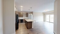 This well-appointed 3-bedroom, 2-bathroom single-floor residence offers a thoughtfully designed open-concept layout. The kitchen and living area flow seamlessly together, anchored by a central island with a light quartz countertop and pendant lighting overhead. Rich dark-stained cabinetry, open shelving, and black appliances — including a refrigerator, range, and dishwasher — give the kitchen a modern yet warm character. Hardwood-style flooring extends throughout the main living areas, while the living room benefits from a sliding glass door that opens to a private balcony, filling the space with natural light.

The primary bedroom is a comfortable retreat, accompanied by an en-suite bathroom featuring a dual-sink vanity with dark cabinetry, quartz countertops, and direct access to a dedicated walk-in closet. The additional bedrooms are carpeted and include window treatments that invite natural light, with one room featuring a built-in closet with bi-fold doors. The second bathroom is equipped with a full tub-shower combo and wood-look tile flooring. A dedicated laundry room with a full-size washer and dryer adds everyday convenience. Neutral tones throughout create a clean, inviting ambiance.
