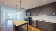 Located at 1904 Reston Metro Plaza in Reston, Virginia, this single-floor residence offers a thoughtfully designed layout that balances modern aesthetics with everyday functionality. The open-concept living and kitchen area is anchored by rich hardwood flooring that extends throughout the main living space, creating a warm and cohesive atmosphere. The kitchen is a standout feature, outfitted with dark espresso-toned cabinetry that reaches toward the ceiling, providing ample storage. A classic white subway tile backsplash contrasts elegantly against the dark cabinetry, while light-toned countertops offer generous prep space. A central kitchen island with pendant lighting above serves as both a functional workspace and a natural gathering point. A full suite of stainless steel appliances, including a gas range, microwave, dishwasher, and refrigerator, completes the kitchen. The living area is open and airy, bathed in natural light with a clean, minimalist design. The bedroom features plush wall-to-wall carpeting and a large window that brings in natural light and exterior views. The bathroom is finished with neutral, travertine-style tile in the tub-shower surround, complemented by light tile flooring and a clean vanity, offering a calm and functional space.