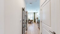 This single-floor residence presents a thoughtfully designed layout that balances functionality with contemporary style. Light wood-tone flooring flows throughout the main living areas, creating a warm, cohesive aesthetic from entry to living room.

Upon entry, a built-in wine rack adds a distinctive decorative touch alongside a convenient coat closet. The corridor leads to a well-equipped kitchen featuring white shaker-style cabinetry extending to the ceiling, granite countertops, a classic subway tile backsplash, and a full suite of stainless steel appliances including a side-by-side refrigerator with ice dispenser, electric range, and built-in microwave.

The living area is bright and welcoming, anchored by a large window dressed with elegant olive-green drape panels and blinds that filter natural light effectively. A ceiling fan overhead adds comfort, while the open layout allows flexible furniture arrangement.

The bedroom offers a calm retreat with plush carpeting, a ceiling fan, and a clerestory window that draws in additional natural light while maintaining privacy.

The bathroom features a soaking tub and shower combination with large-format grey tile surround, wood-tone flooring, and clean white fixtures, completing this well-rounded residence.