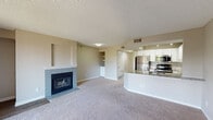 This single-floor unit offers a well-organized layout that balances open communal spaces with comfortable private areas. The living room serves as the centerpiece, featuring a tile-surround gas fireplace with a white mantle and built-in shelving nearby, providing both warmth and functional display space. Plush neutral carpeting extends throughout the living areas and bedrooms, contributing to a cozy atmosphere. A sliding glass door connects the living room to a private balcony, allowing natural light to fill the space and offering outdoor views of surrounding trees.

The kitchen is thoughtfully designed with white cabinetry, granite countertops, wood-look flooring, and a full suite of stainless steel appliances, including a refrigerator, range, microwave, and dishwasher. A curved peninsula with a granite surface separates the kitchen from the living area, creating a practical and visually distinct transition between the two spaces.

The bedrooms are carpeted and receive natural light through large windows with outdoor views. One bedroom includes a walk-in closet for generous storage. The bathroom features a tiled tub-shower combination with a warm accent tile border, wood-look flooring, and a granite-topped vanity, completing the unit's cohesive aesthetic.